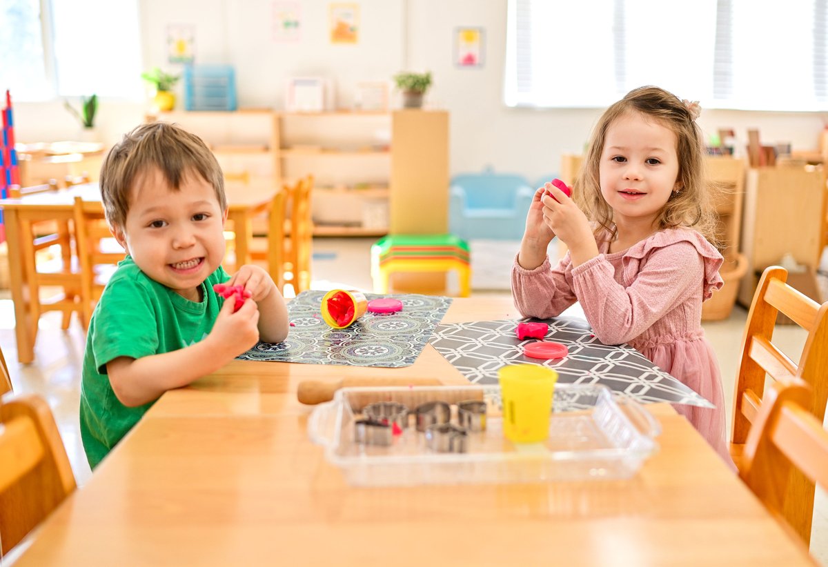Two smiling children playing with clay and playdough at table
