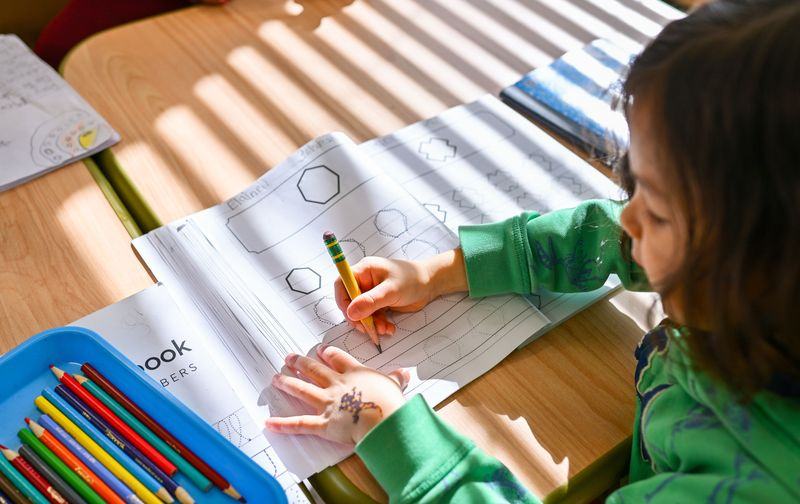 Child focused on writing and drawing in Montessori workbook