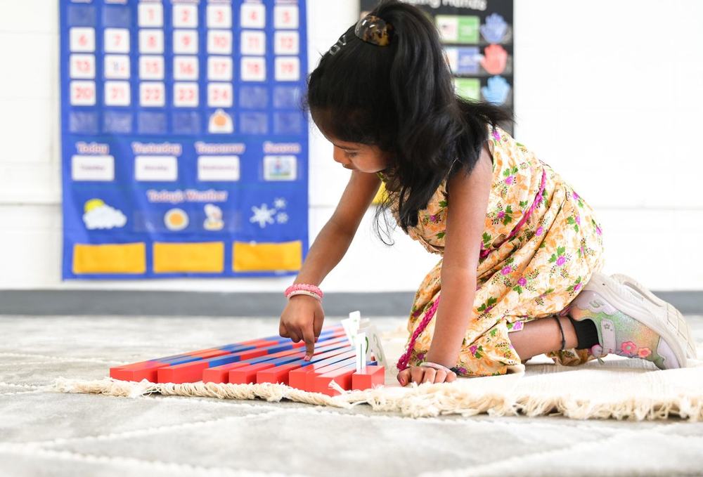Child arranging the red and blue Montessori Number Rods on a floor mat