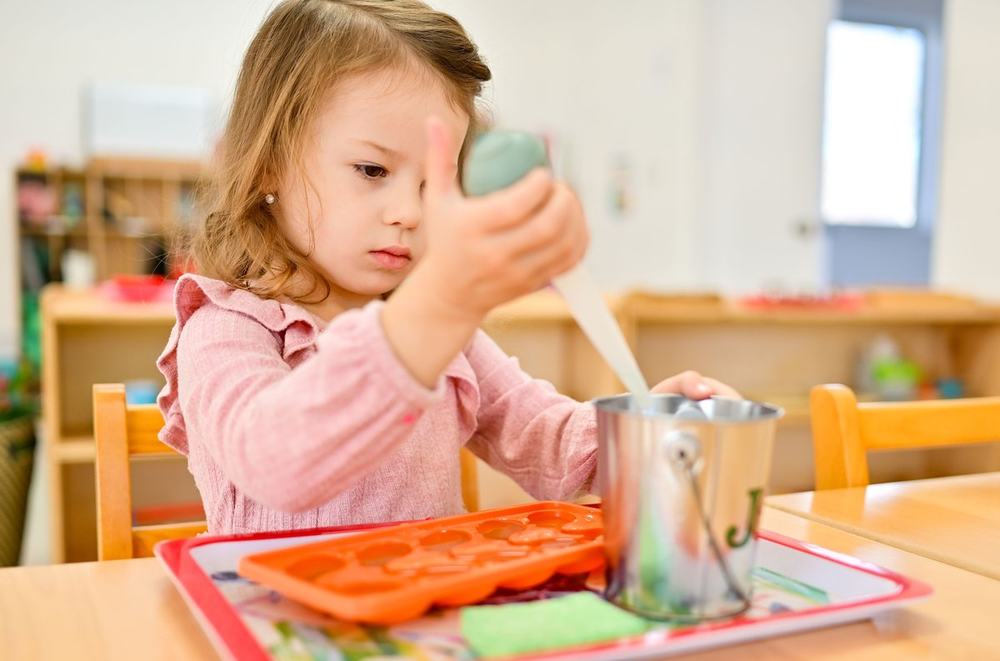Child carefully transferring water with a dropper into an ice-cube tray