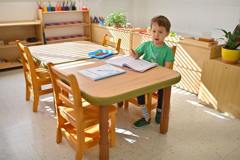 Sunlit Milestones Montessori classroom with natural wood tables, low open shelves, and plants