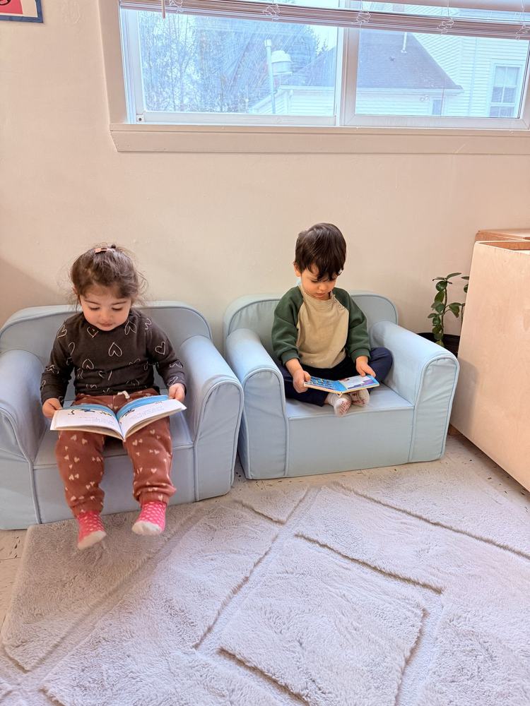 Two young children reading picture books in the cozy reading corner