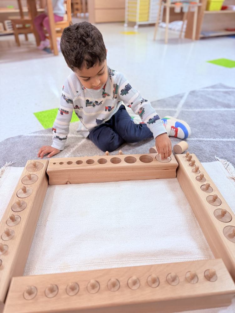 Child working with four sets of Montessori Knobbed Cylinders on a floor mat